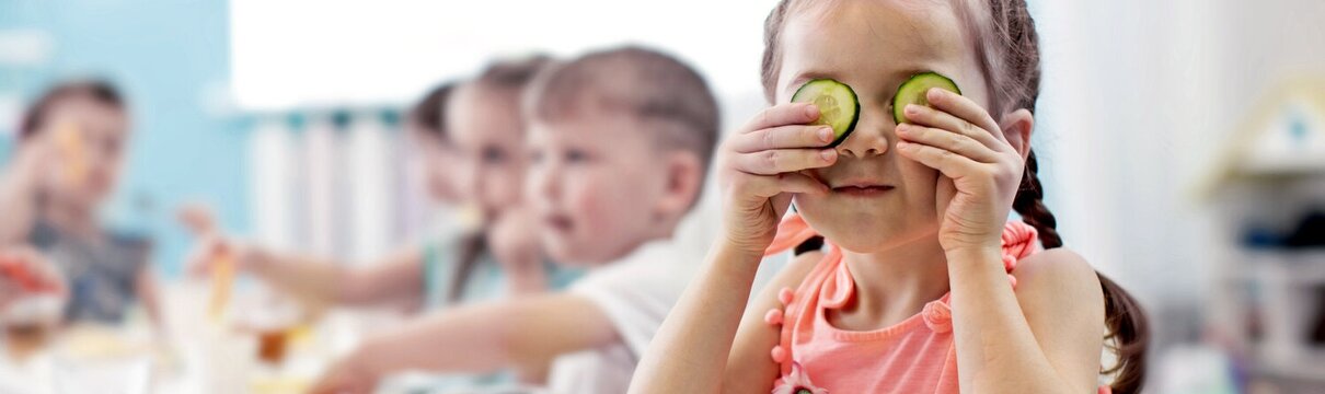 Óvodás kislány játékosan uborkát tart az arcába